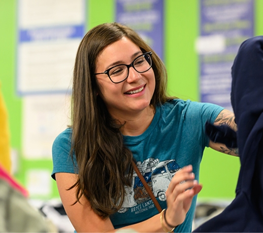 Smiling woman with glasses helping a student in a bright classroom