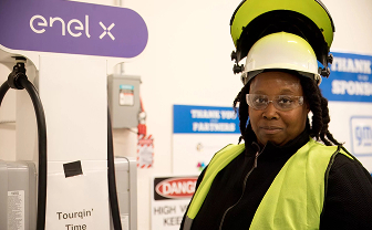 Worker wearing a yellow high-visibility vest and helmet at an Enel X facility.