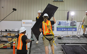 Workers in safety gear install a solar panel on a roof during a training session.
