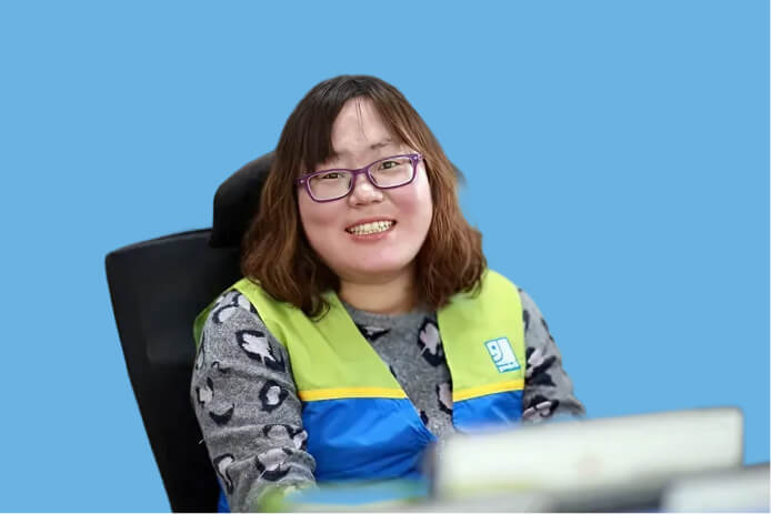 Smiling woman with purple glasses wearing a lime-green and blue safety vest sits at a desk against a blue background.