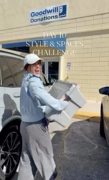 Person wearing a white cap carries a large box beside a Goodwill donation center.