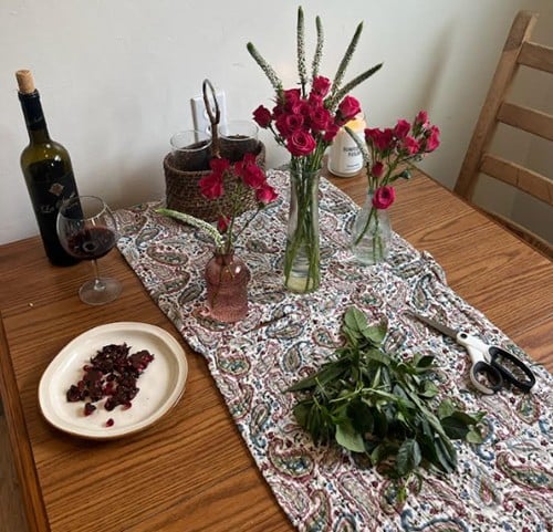 Table with a paisley-patterned runner, a wine bottle and glasses, and multiple bouquets in vases.
