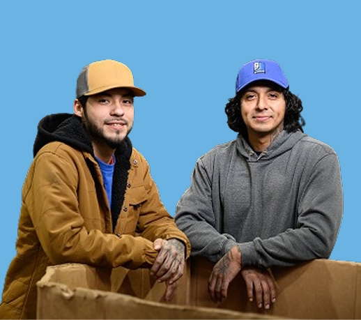 Two men leaning on a cardboard box against a blue backdrop.