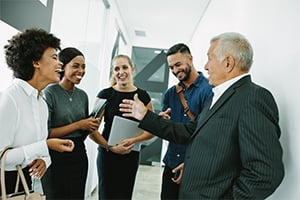 Diverse group of professionals in a modern office discussing a presentation as an older man in a suit speaks.