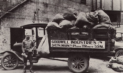 Vintage Goodwill Industries truck loaded with sacks beside a brick building, with a worker standing nearby.