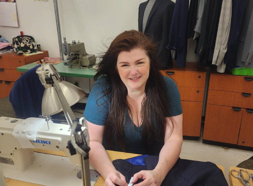 Smiling woman sewing fabric at a Juki sewing machine in a garment workshop.
