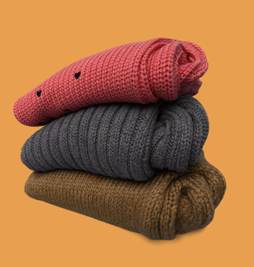 Stacked knitted sweaters in pink, gray, and brown on an orange background.