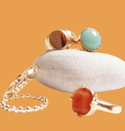 Gold jewelry with green and orange gemstones displayed on a smooth gray stone against an orange backdrop.