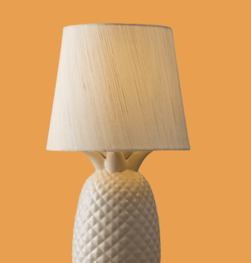 White ceramic lamp with a quilted, textured base and beige fabric shade on an orange background.